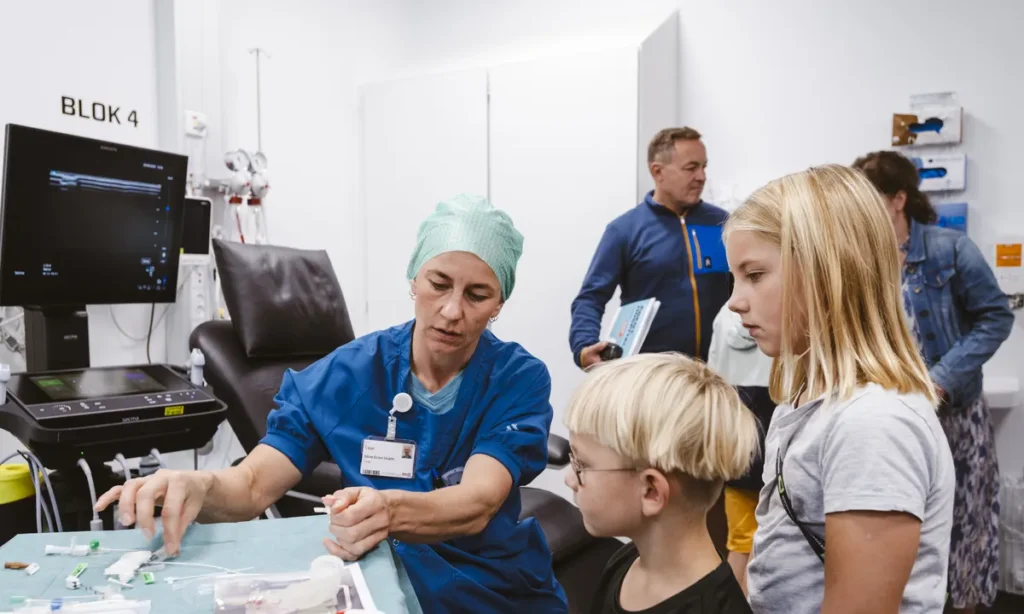 Læge i operationstøj demonstrerer medicinsk udstyr for børn ved Åbent Hospital arrangement